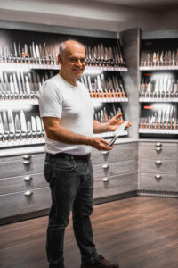 Inhaber der Messerschmiede Kneissler in Zell am Harmersbach präsentiert ein Messer vor der großen Ausstellungswand mit hunderten Messern